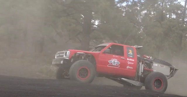 A red truck is driving down a dirt road.