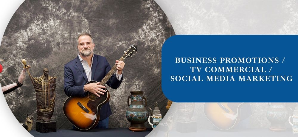 A man is holding a guitar in front of a sign that says business promotions tv commercial social media marketing