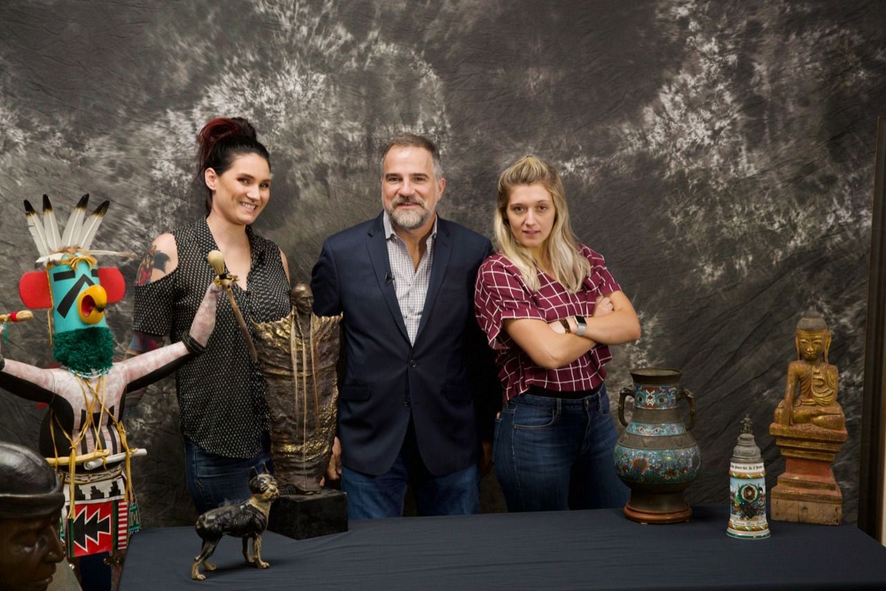 A man and two women are posing for a picture in front of a table filled with sculptures.
