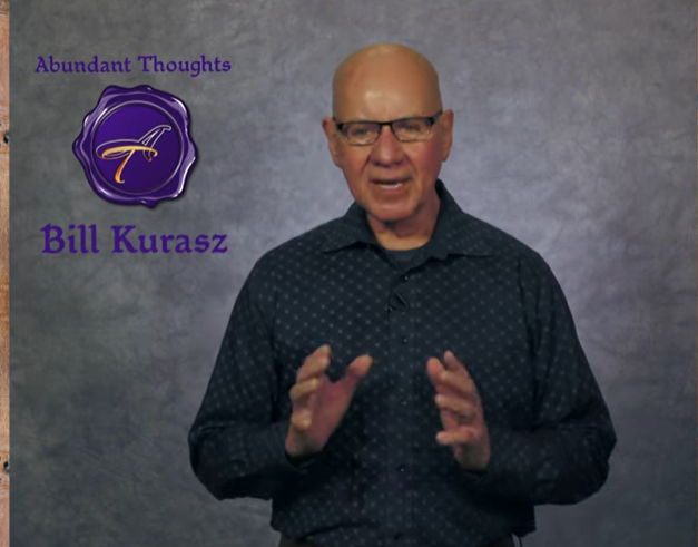 A bald man wearing glasses stands in front of a sign that says bill kurasz