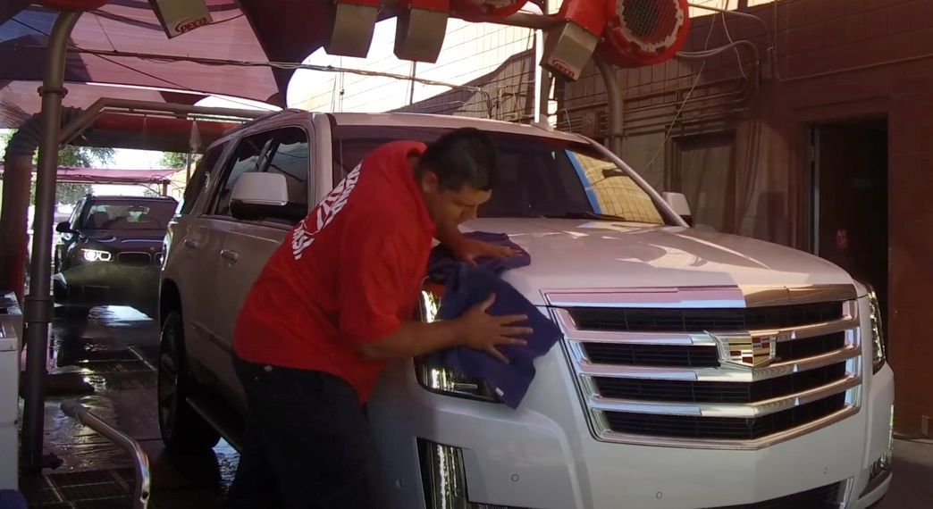 A man in a red shirt is washing a white car.