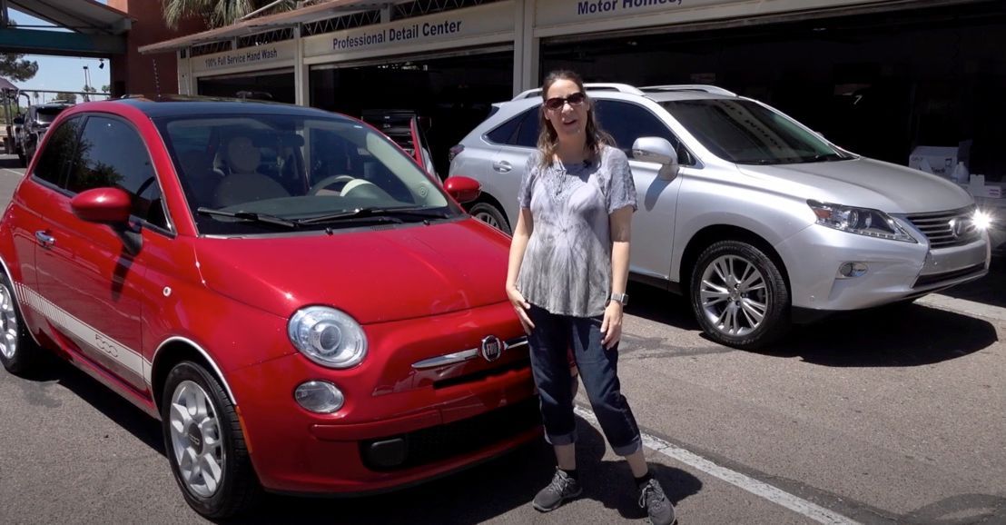 A woman is standing in front of a red car and a silver car.
