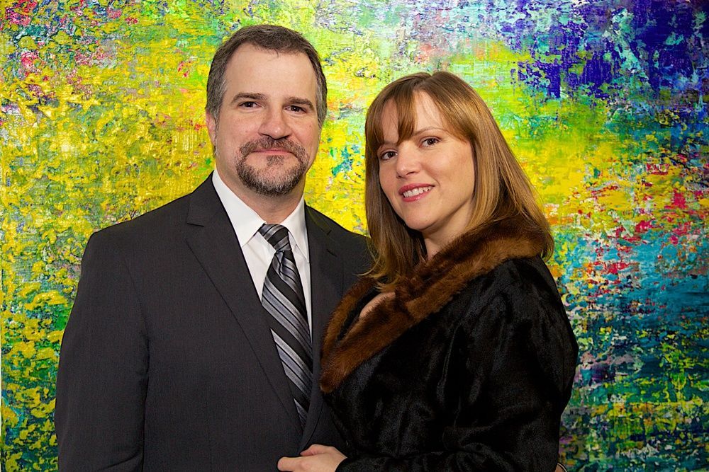 A man and a woman are posing for a picture in front of a colorful painting.