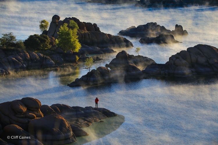 A person is standing on a rock in the middle of a lake.