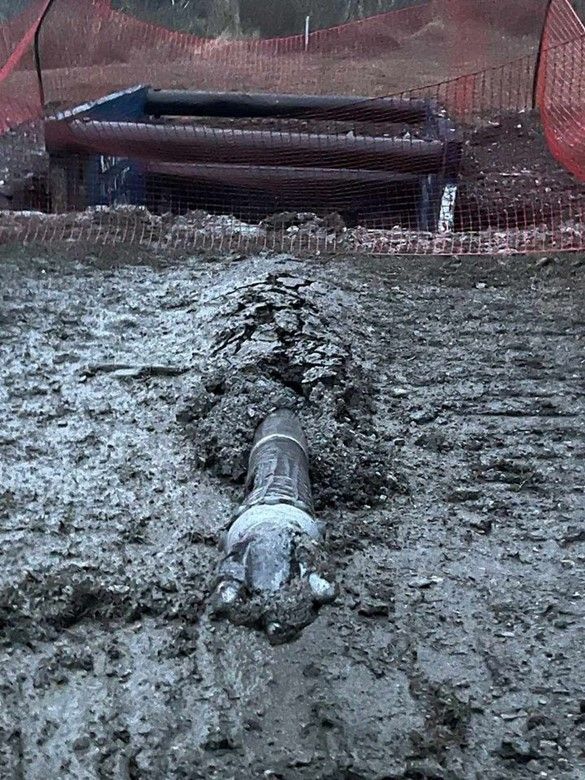 A man is standing next to a large pipe in the dirt.