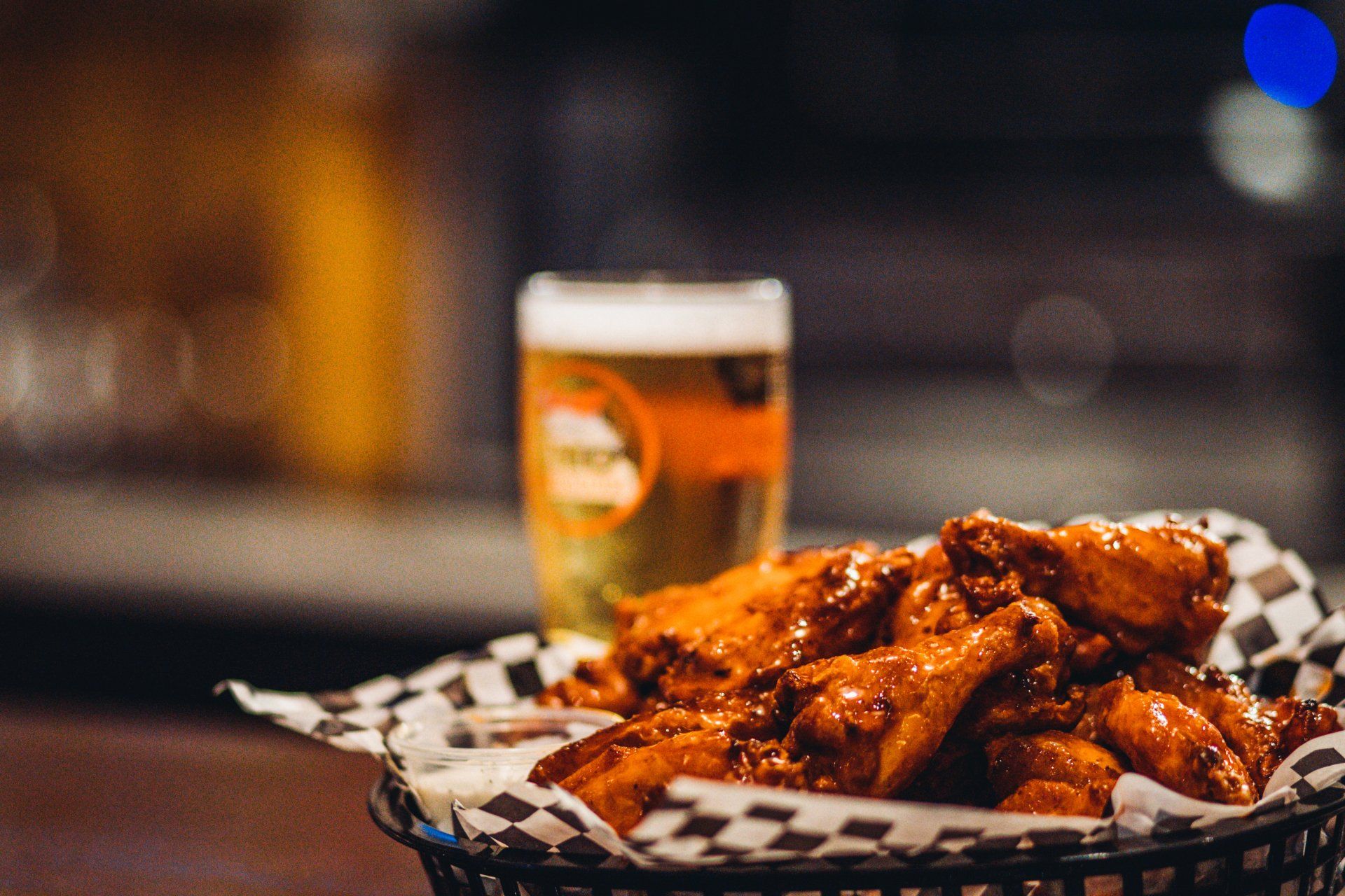 A basket of chicken wings and a glass of beer on a table.