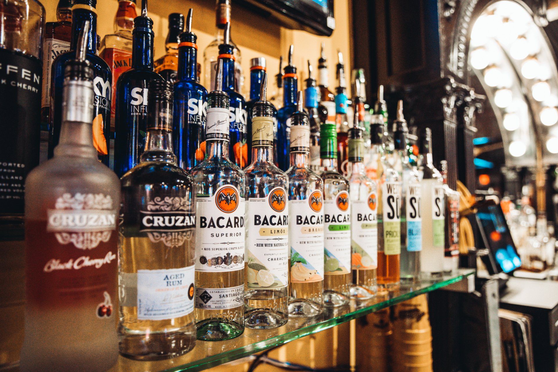 A row of liquor bottles are lined up on a glass shelf.