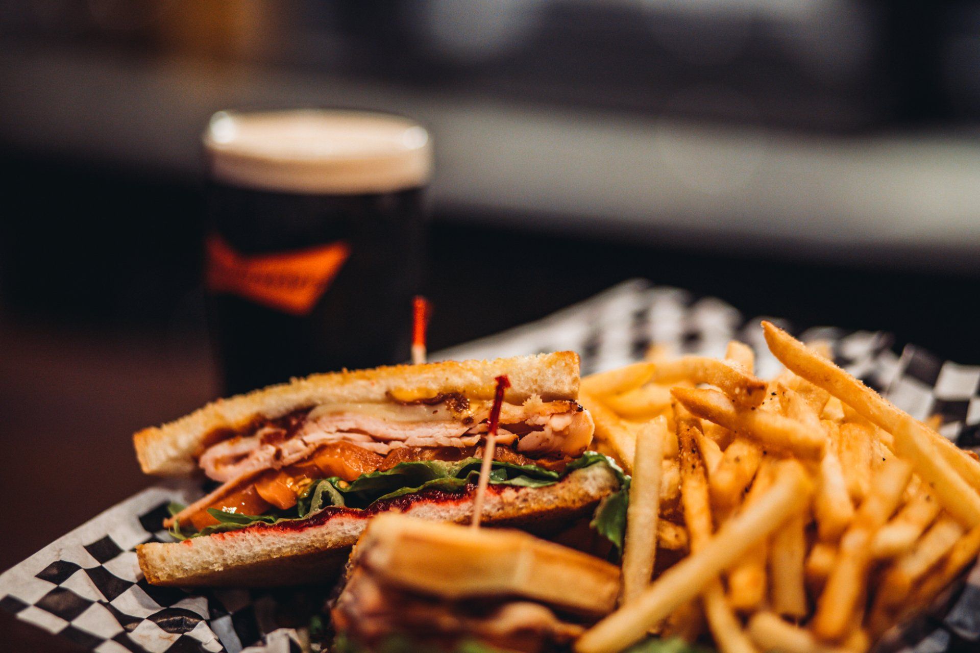 A club sandwich and french fries on a plate with a glass of beer in the background.