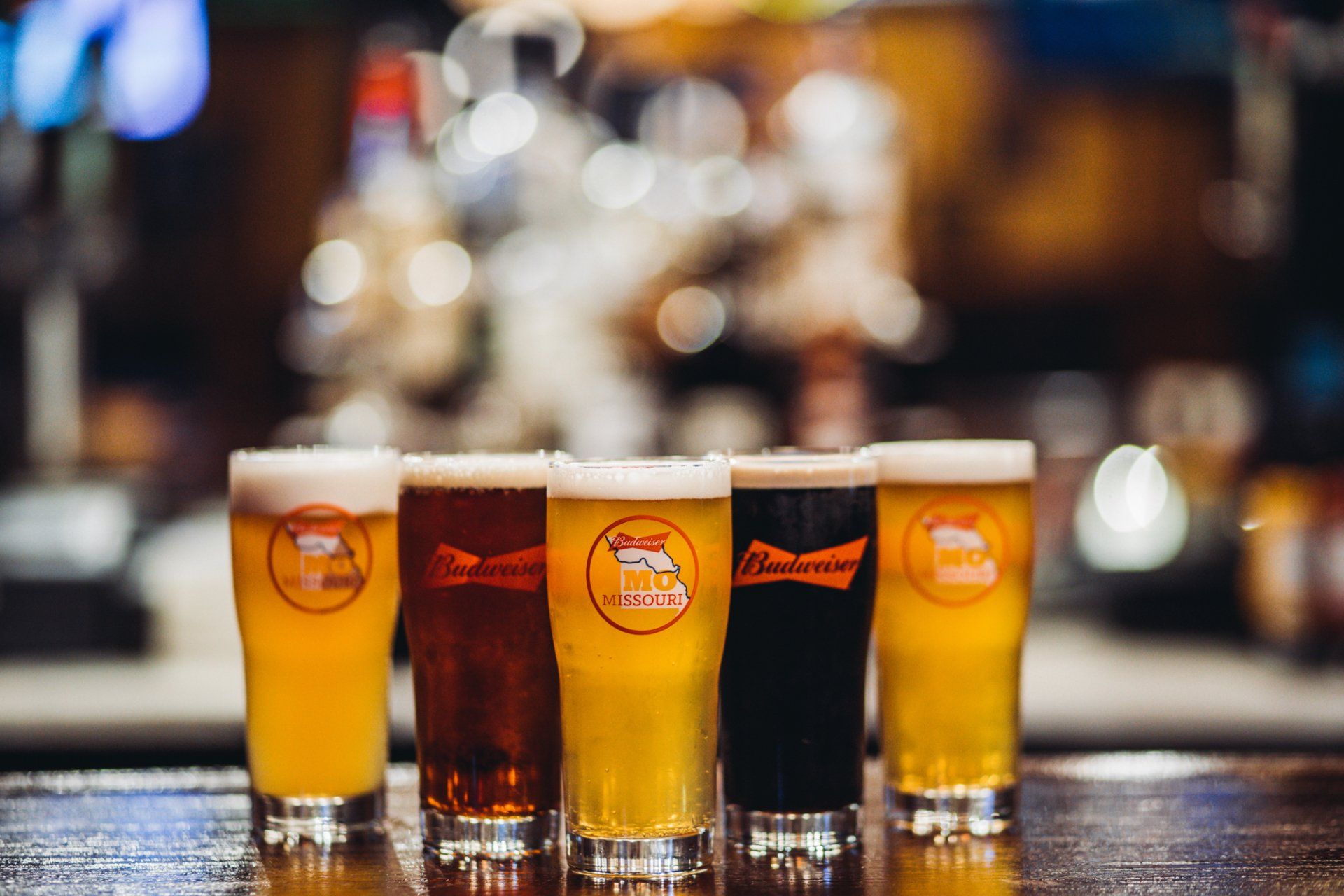 A row of beer glasses filled with different types of beer are sitting on a bar.