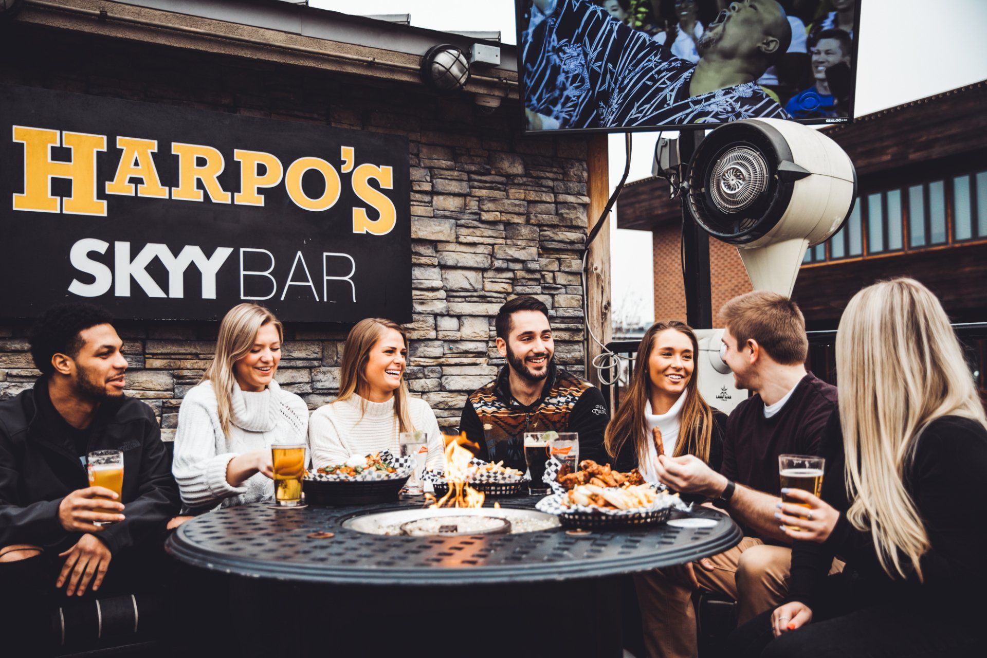 A group of people are sitting at a table in front of a sign that says harpo 's sky bar.