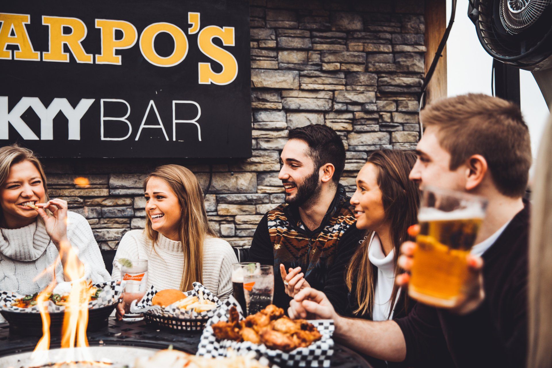 A group of people are sitting at a table eating food and drinking beer.