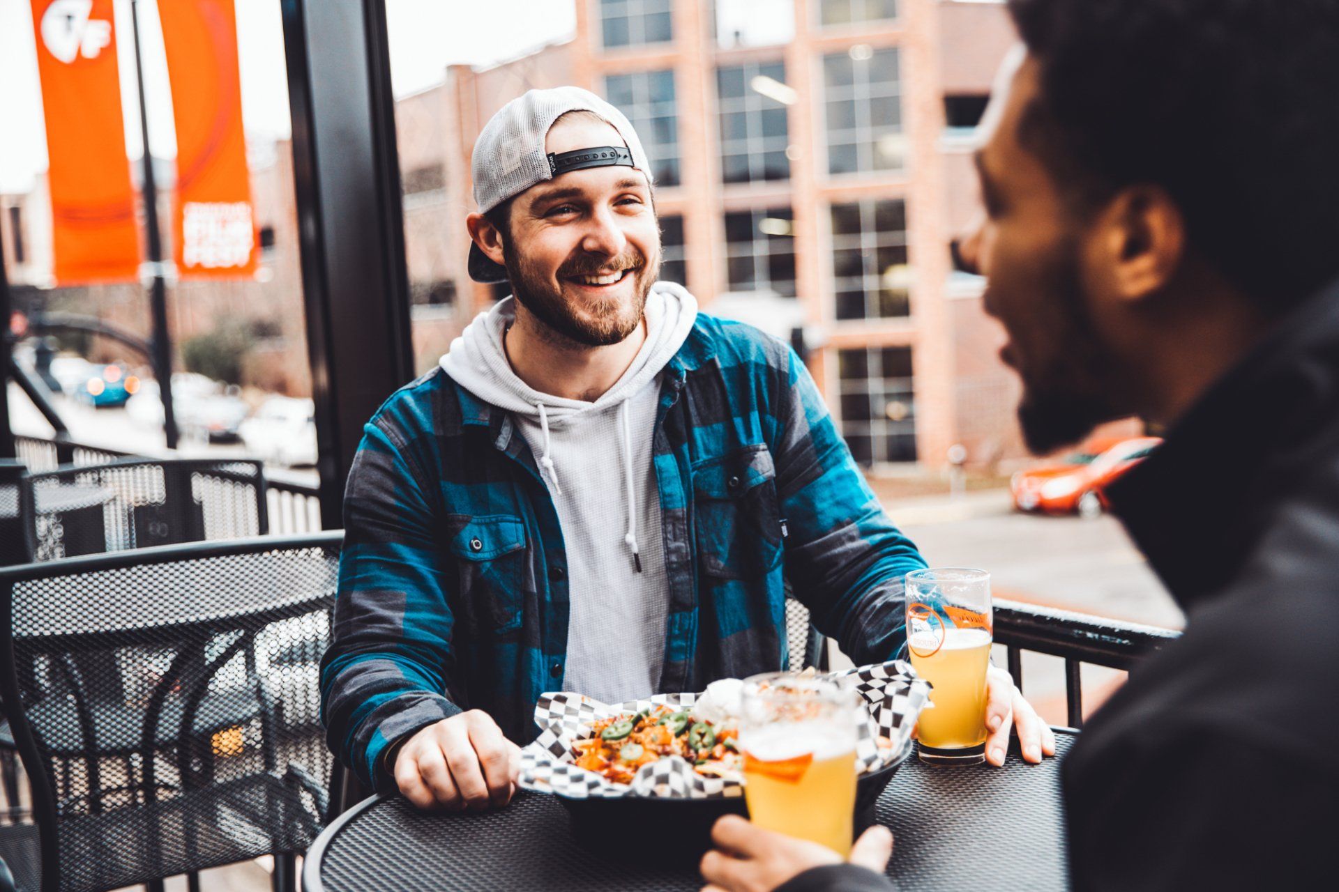 Two men are sitting at a table eating food and drinking beer.