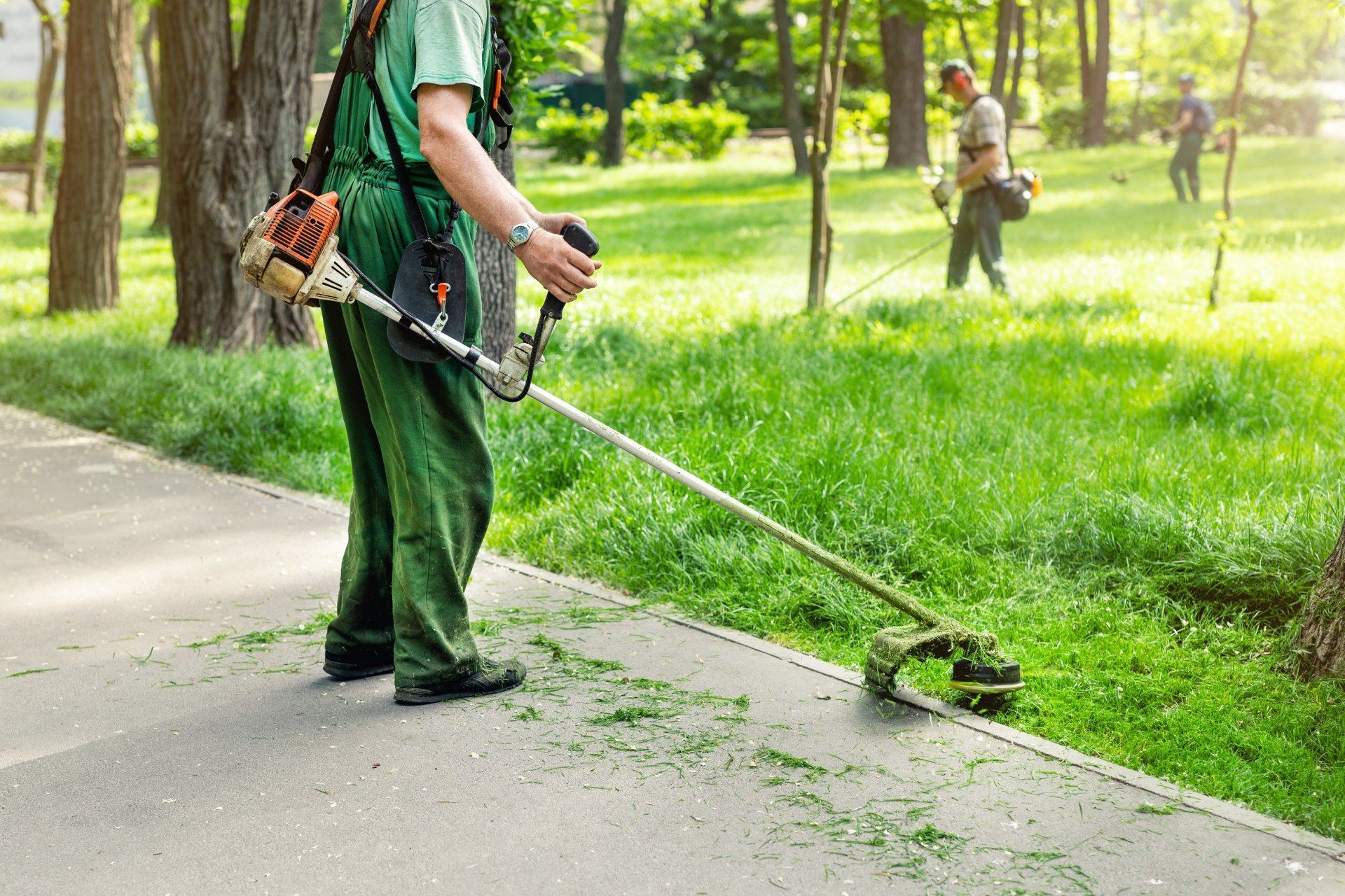 A man is using a lawn mower to cut grass in a park.