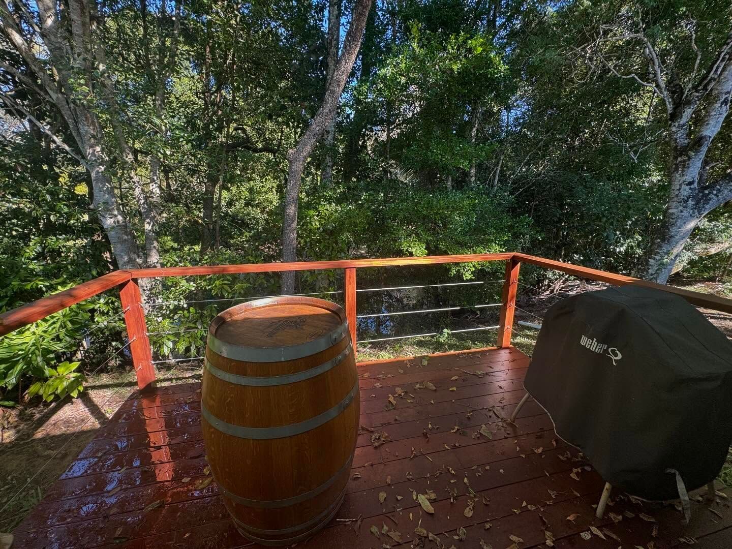 Wooden barrel and grill on a wooden deck with a red railing, surrounded by trees and foliage.