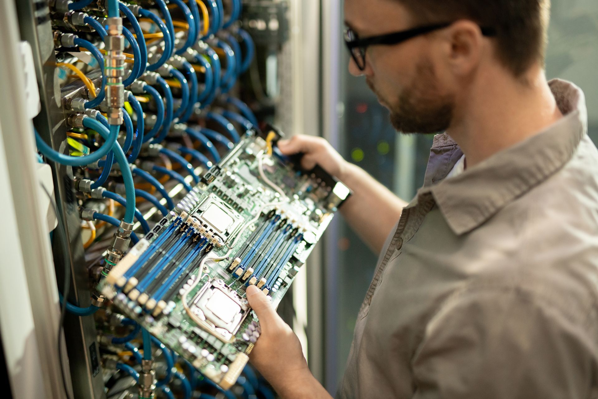 Man inspecting a circuit board in a server room, surrounded by cables.