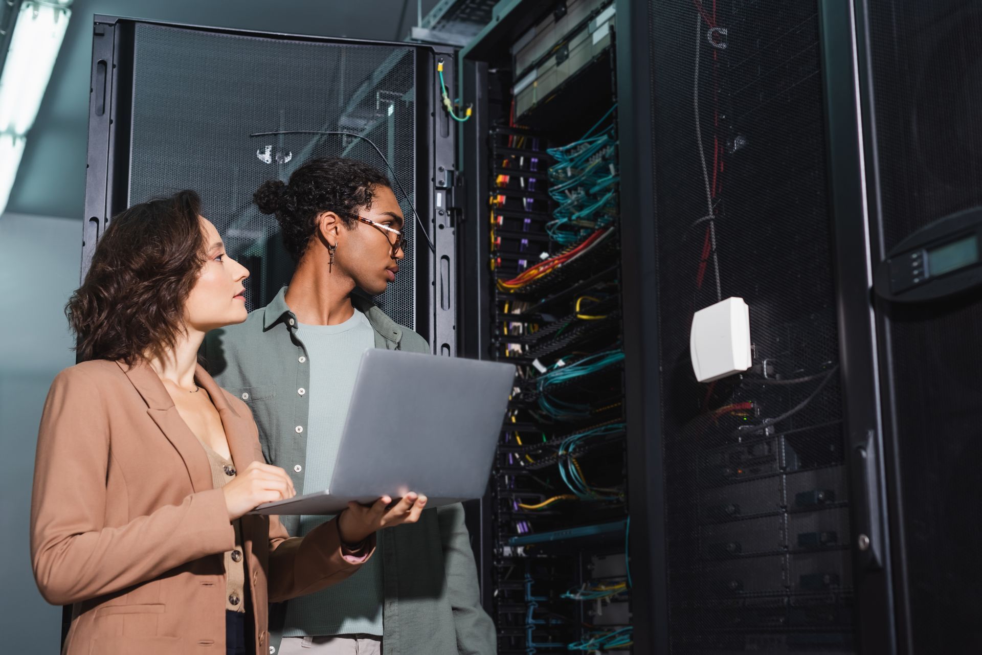 Two people inspecting server racks with a laptop in a data center.