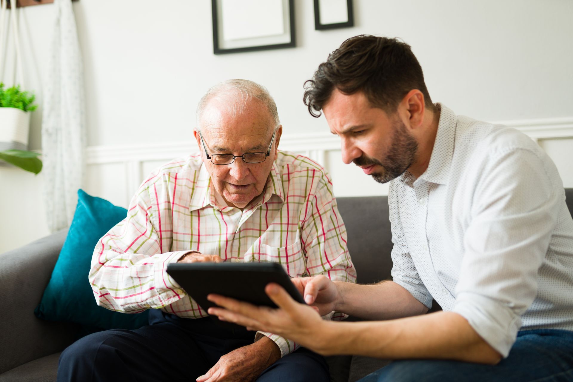 An older adult and a younger person looking at a tablet together on a couch.