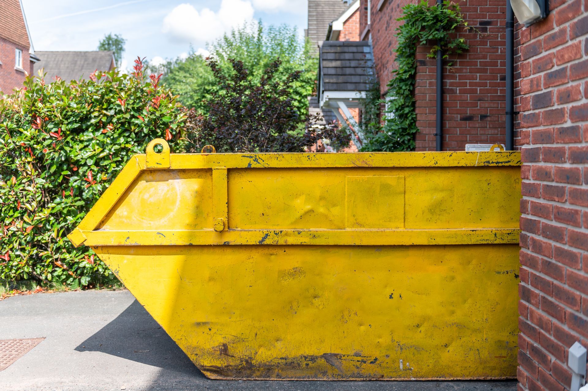 Yellow Dumpster on A Driveway Next to A Brick Building and Green Bushes — UBIN in Ballina, NSW