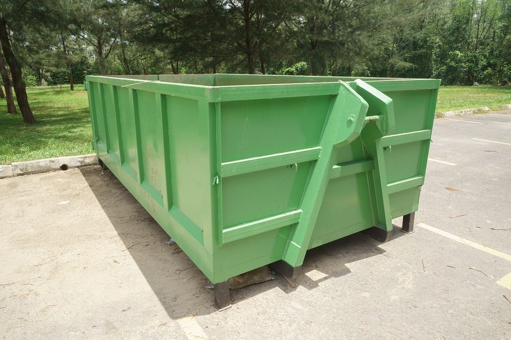 Green Metal Dumpster on A Paved Area with Trees and Grass in The Background — UBIN in Broadwater, NSW