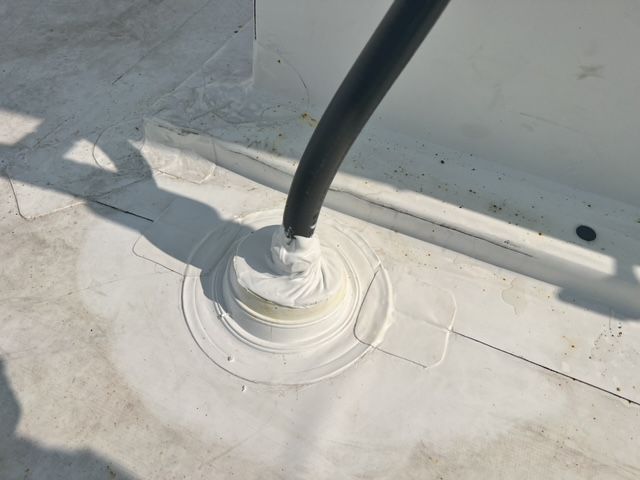 A black hose is sticking out of a hole in a white roof.