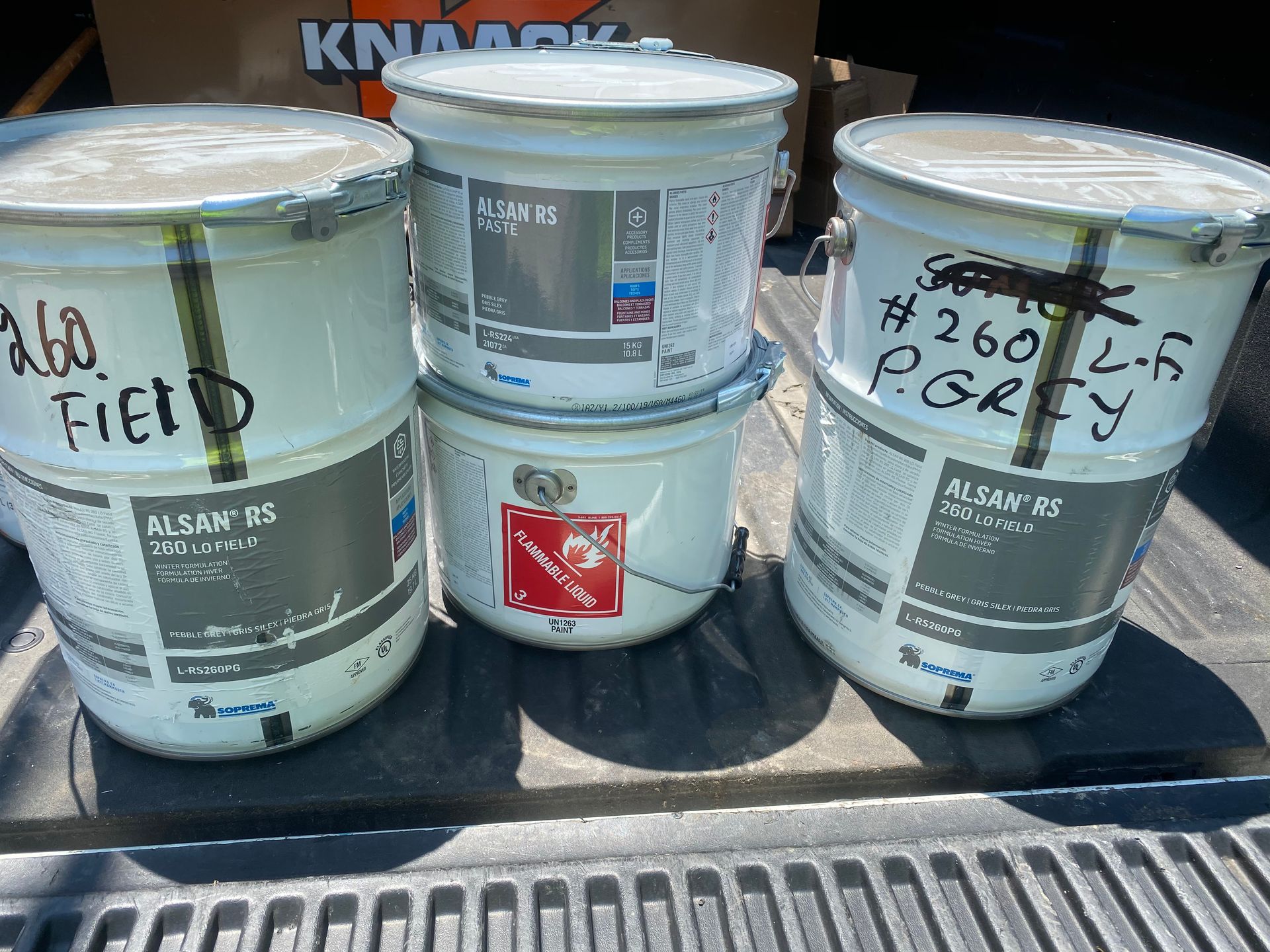 Three buckets of paint are stacked on top of each other on a truck bed.