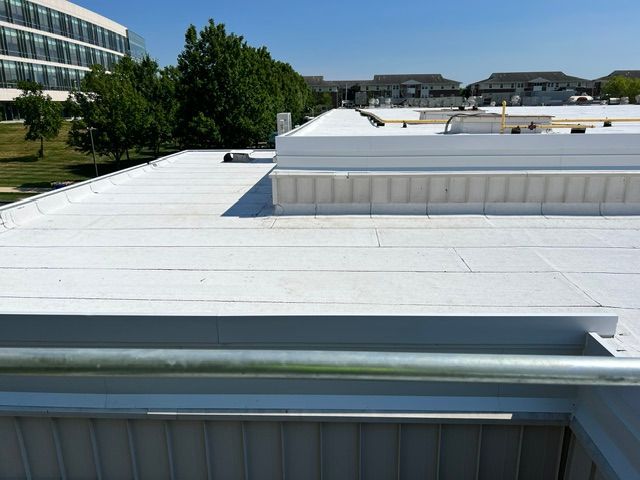 The roof of a building with a white roof and trees in the background.