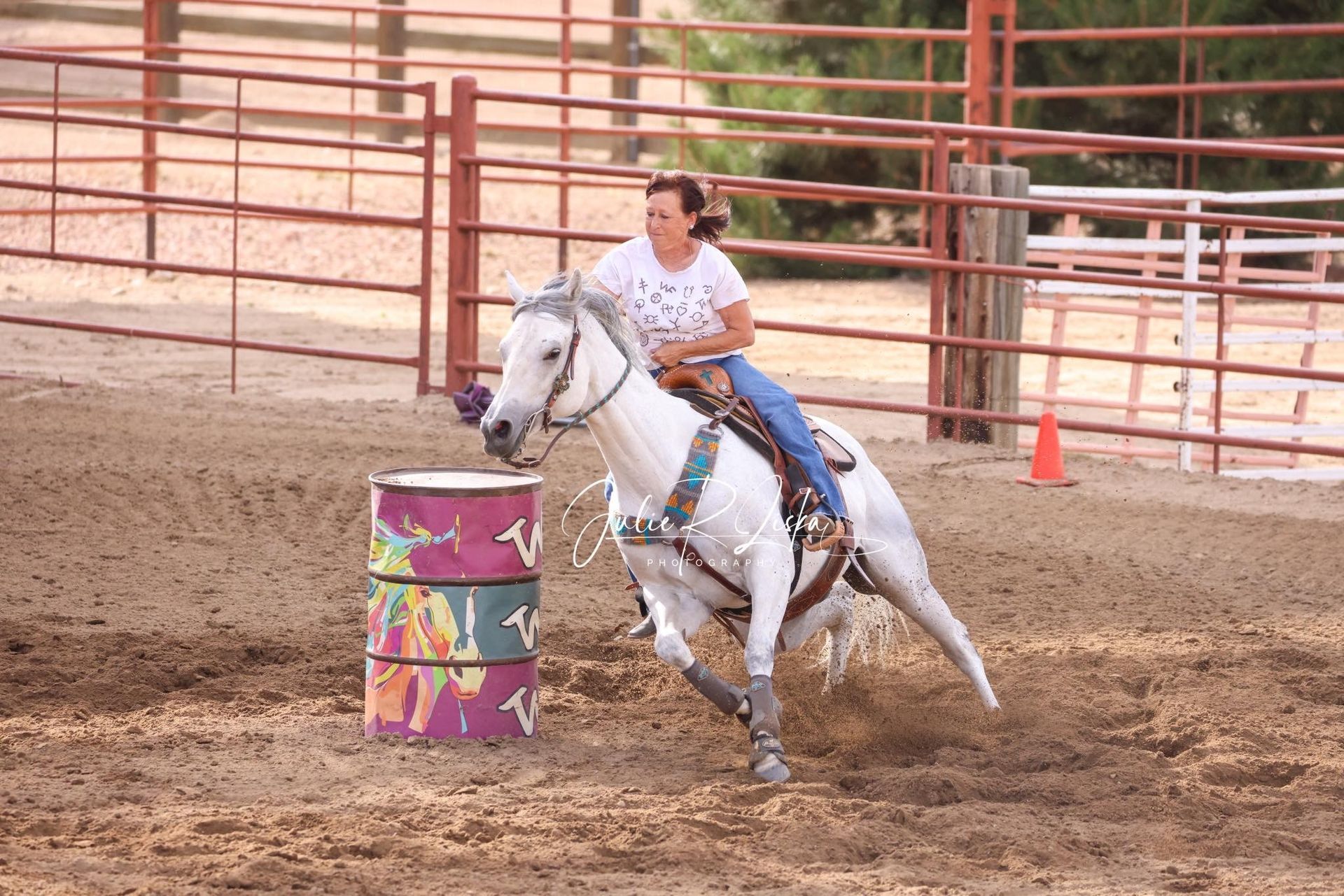 A woman is riding a white horse around a colorful barrel.