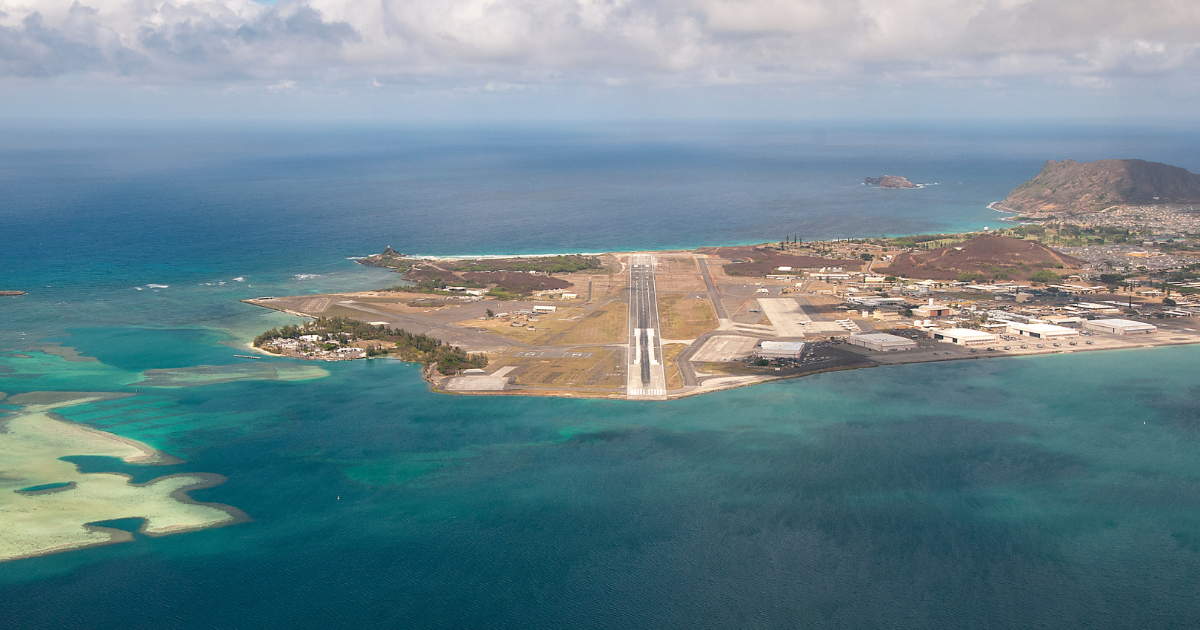 Aerial view of a runway surrounded by turquoise water and a coastal cityscape under a cloudy sky.