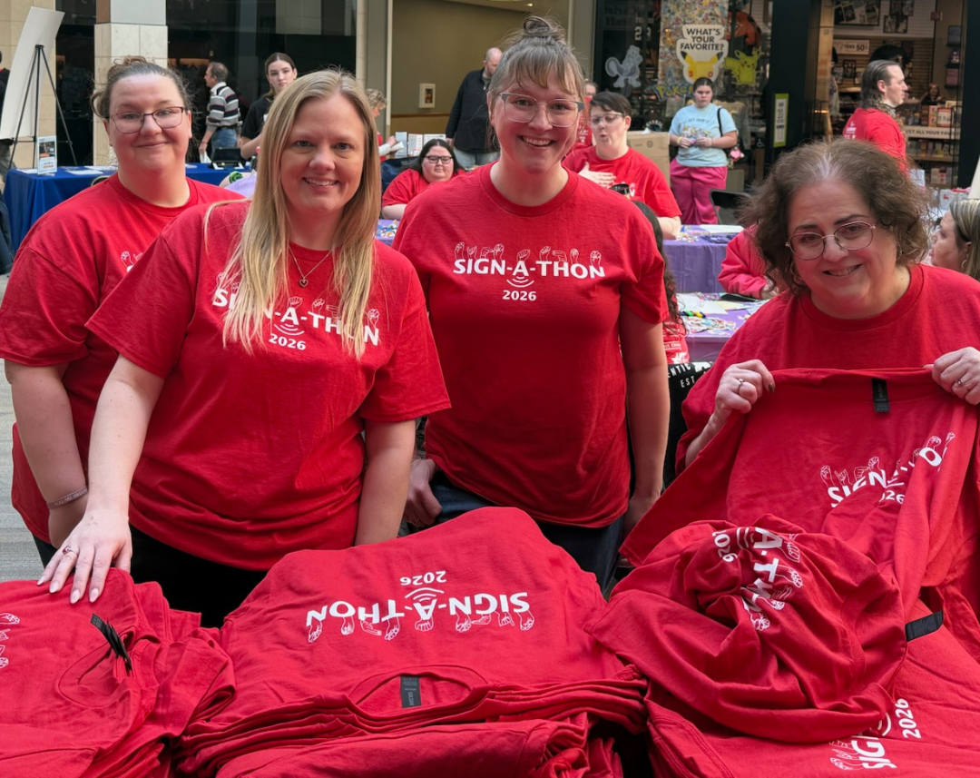 Group of people in purple shirts cheer with gold pom-poms at an indoor event.