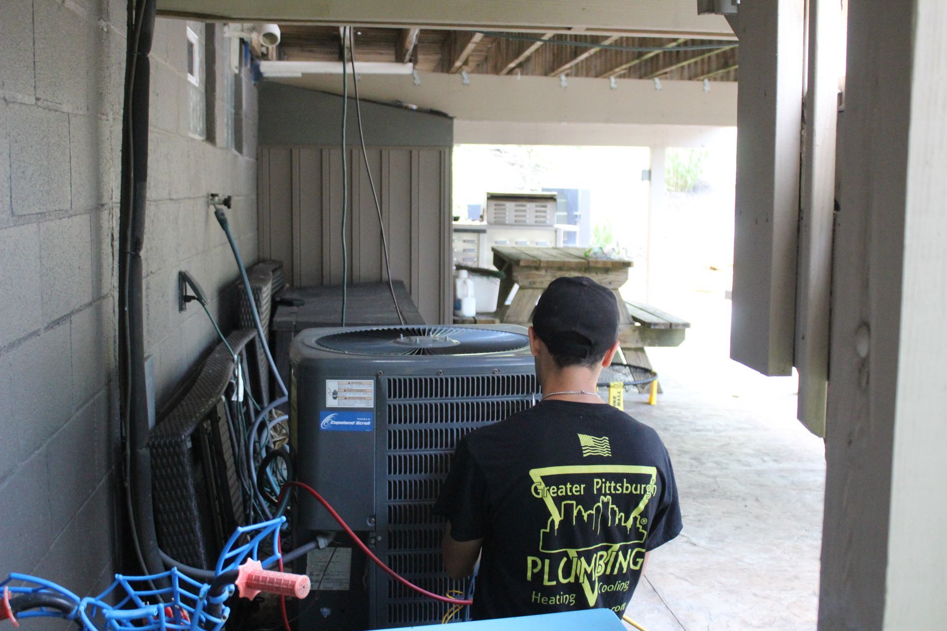 Two men are working on an air conditioner outside of a brick building.