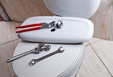 A toilet with a wrench and pliers on top of it.