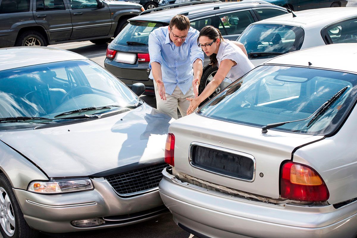 Two frustrated drivers examining front and rear bumper damage after a parking lot car accident, show
