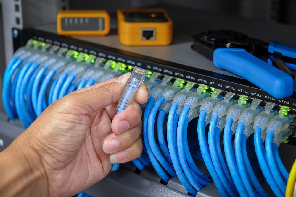 Hand Of System Administrator With Network Cable Connected To Patch Panel Of Network Gigabit Switch — 7E Integrated Services In Port Stephens NSW