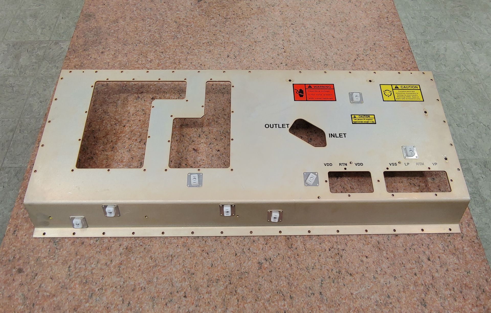Tan metal equipment panel with cutouts, holes, and labels on a wood surface.