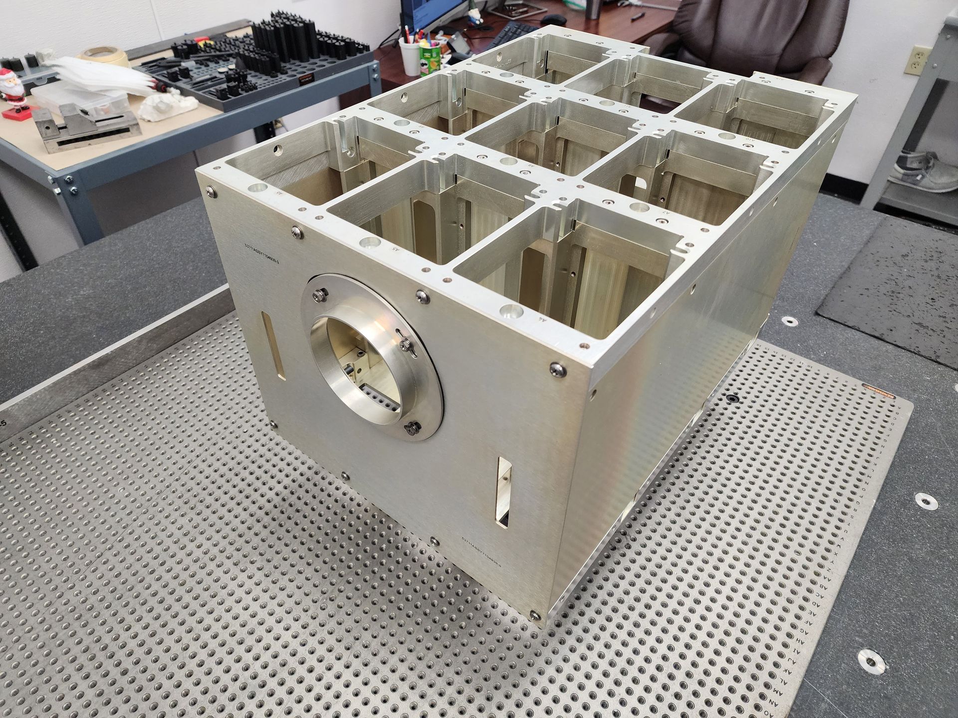 Silver metal rectangular device with internal compartments, possibly for scientific use, on a metal surface.