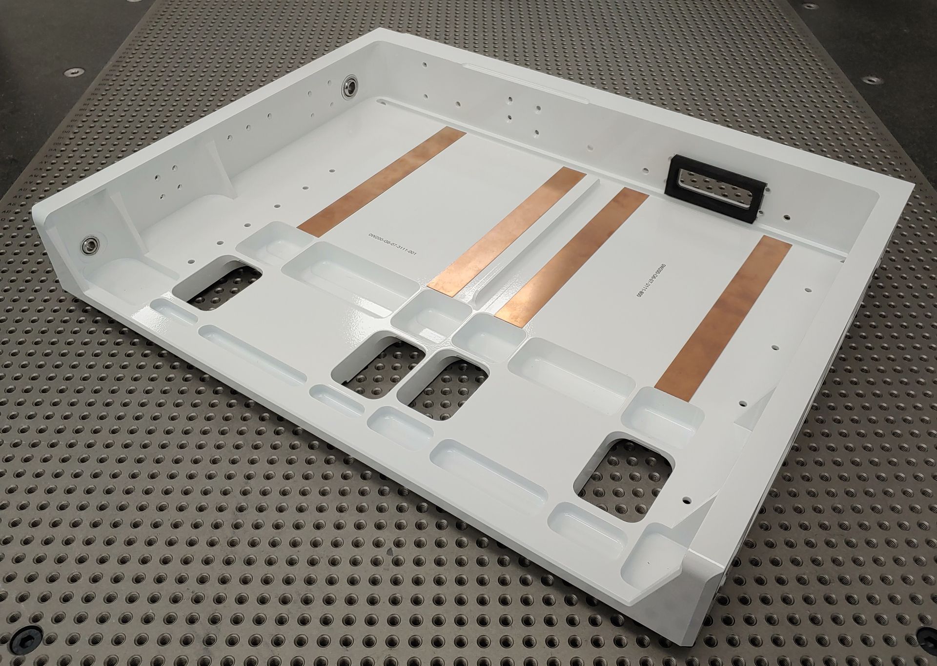 White rectangular plastic component with copper strips and rectangular cutouts on a metal surface.