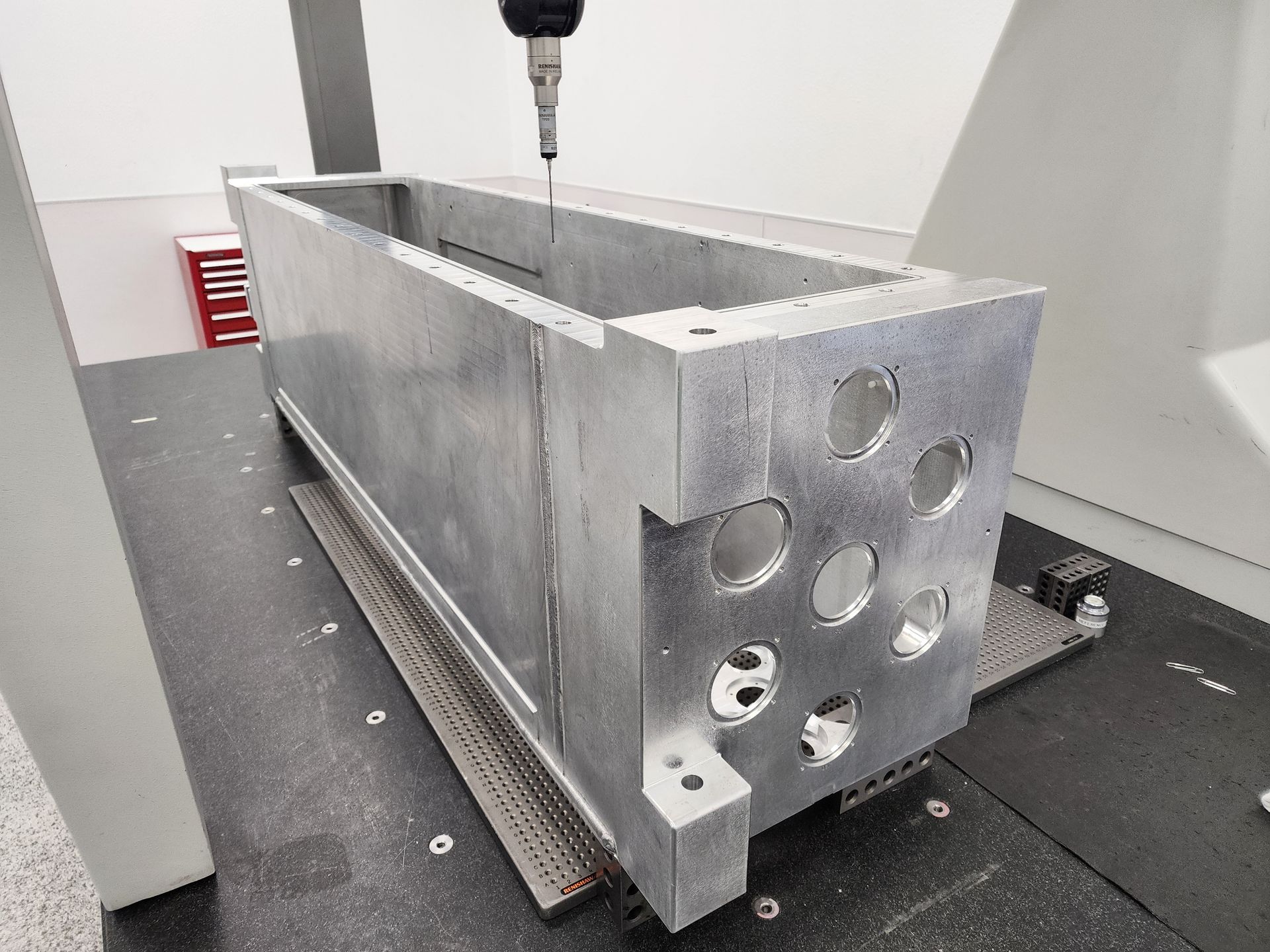 A metal rectangular part on a measurement machine, being inspected with a probe.