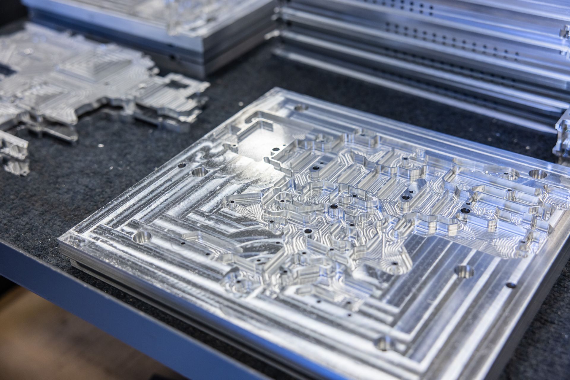 Metal plates with intricate geometric designs, likely manufactured, on a dark table, with others stacked in the background.
