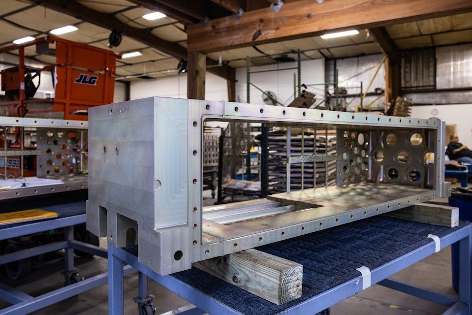 Large metal rectangular frame in a workshop, on wooden supports, with many holes.