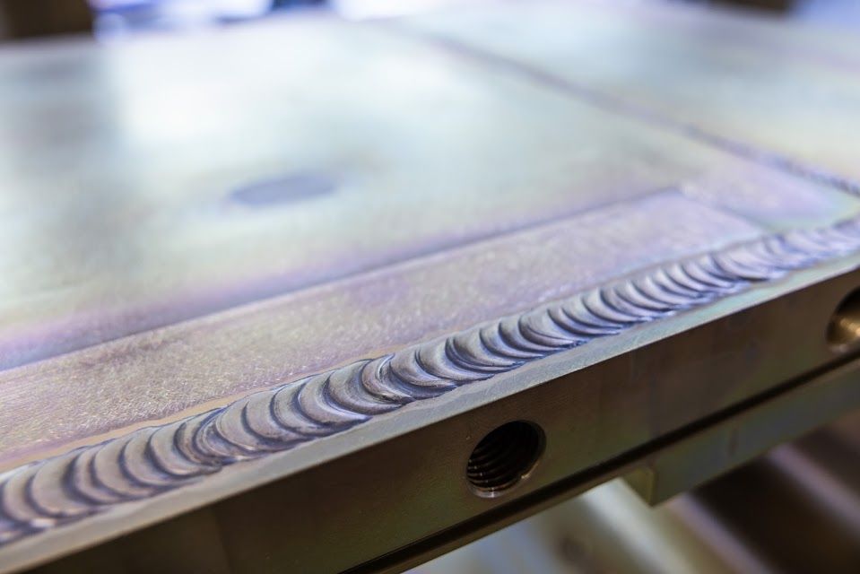 Close-up of a metal surface with a neatly welded seam, showing a row of overlapping crescent-shaped welds.