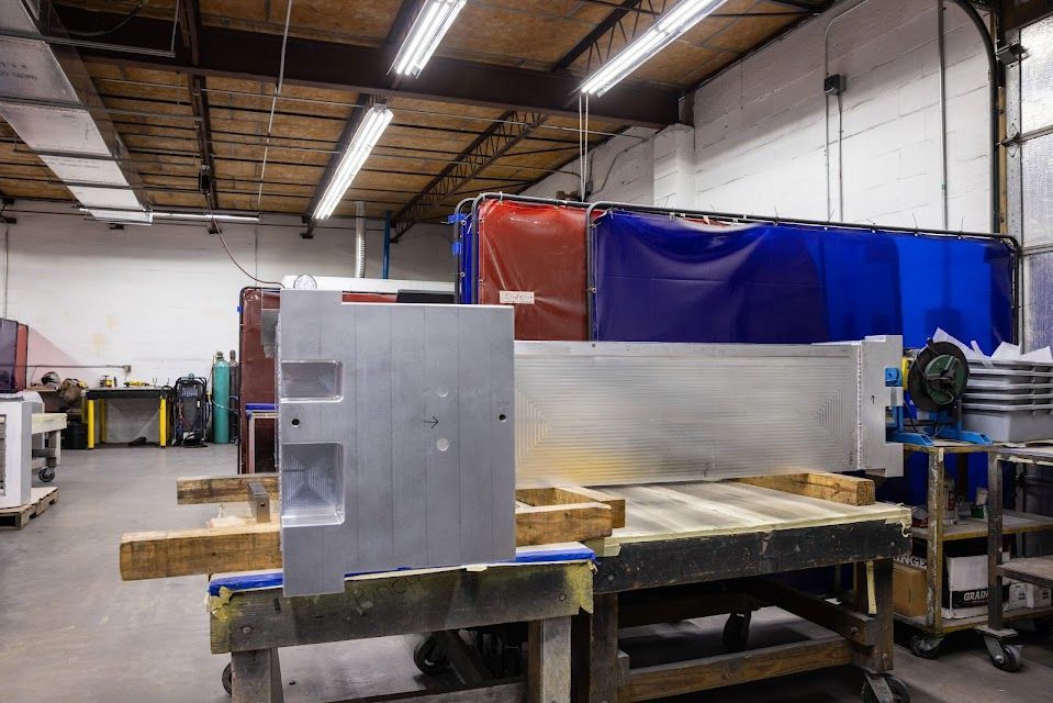 Metalwork shop with a large metal panel in the foreground and welding curtains in the background.