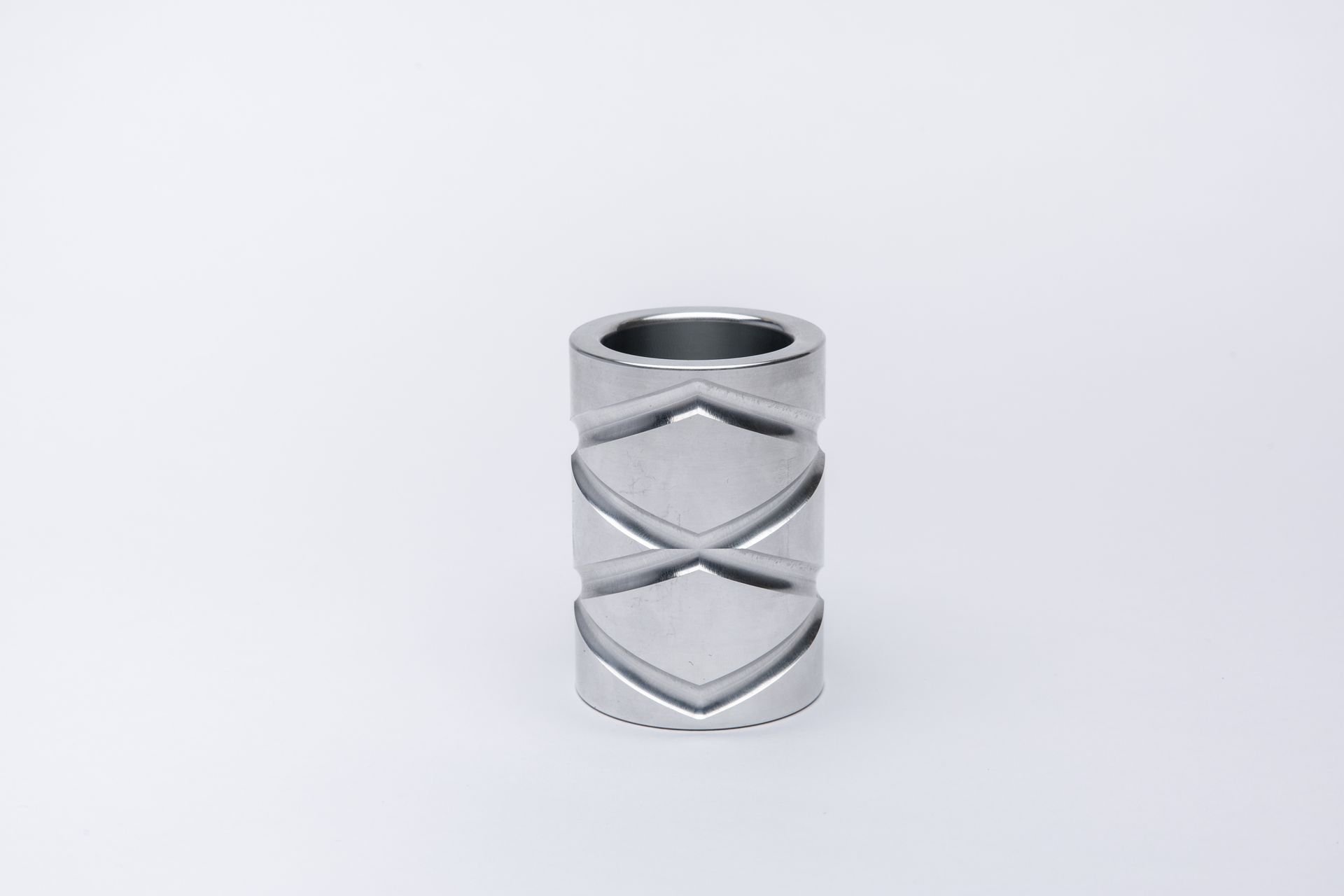 Cylindrical metal object with decorative geometric cutouts, resting against a white background.