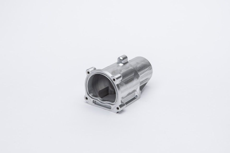 Silver-colored, cylindrical metal part with a hollow interior and multiple mounting holes.
