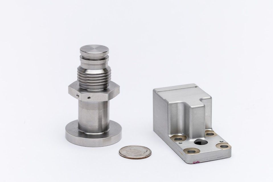 Two metal machine parts and a coin on a white surface.