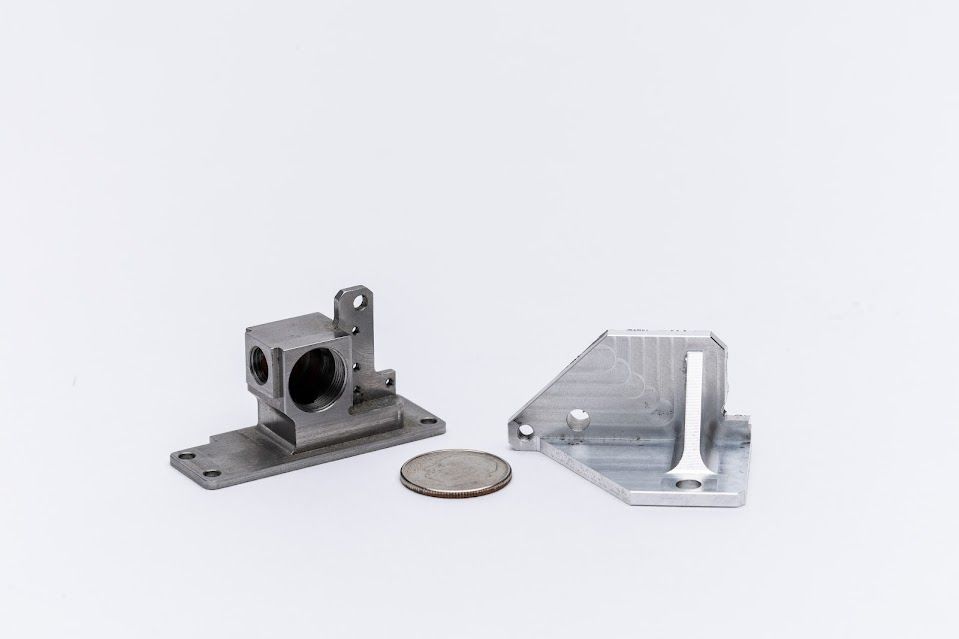 Two silver metal machined parts with a quarter for scale.