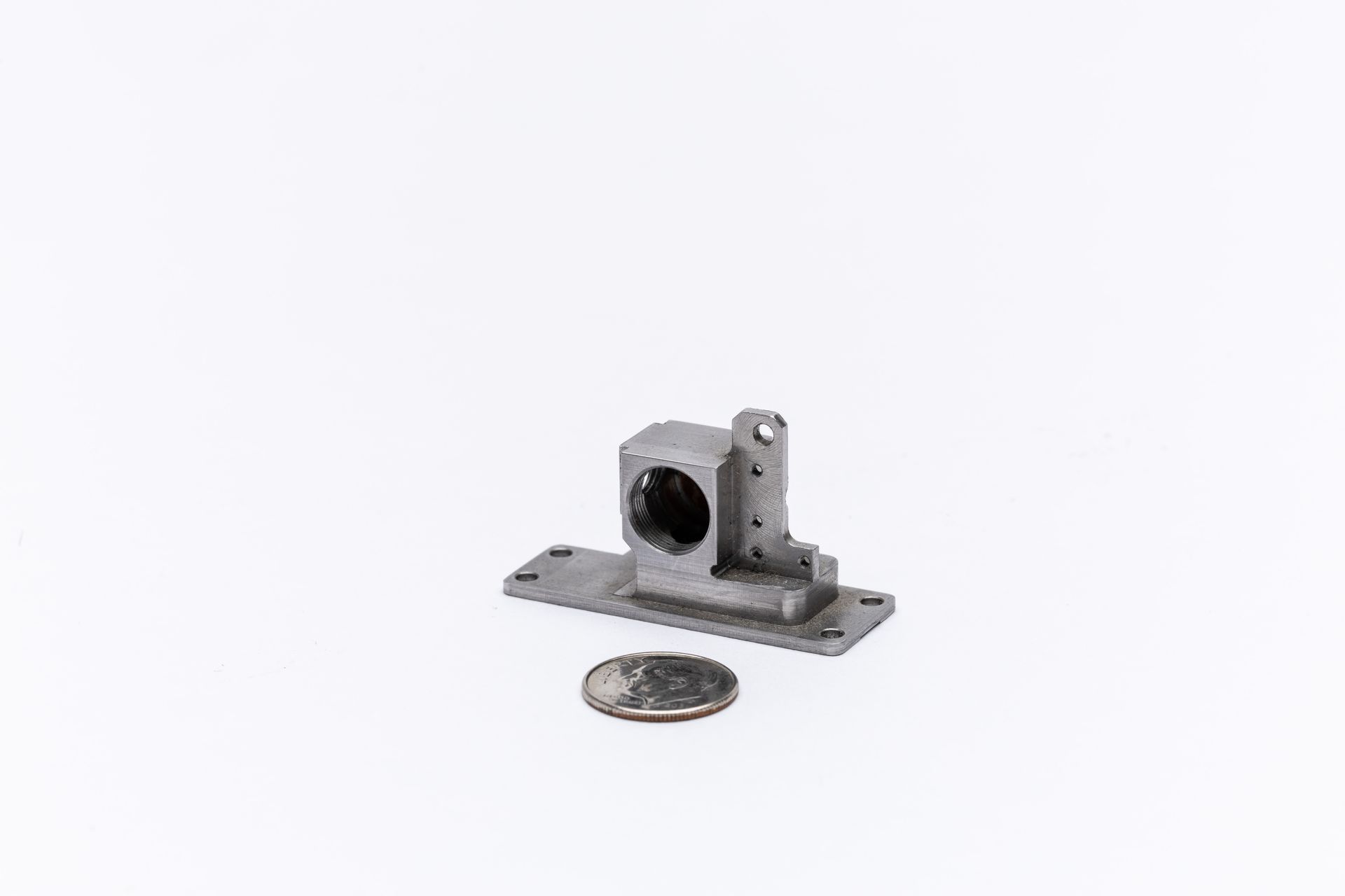 Small metal bracket with a circular hole, rectangular base, and a U.S. quarter for scale.