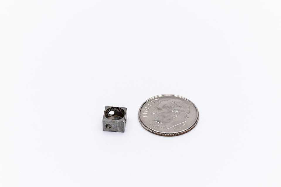 Small, dark, cubed object with a rounded indentation next to a quarter, on a white surface.