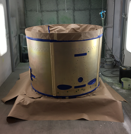 Large, cylindrical metal object, taped and masked, in a spray painting booth, ready for paint.