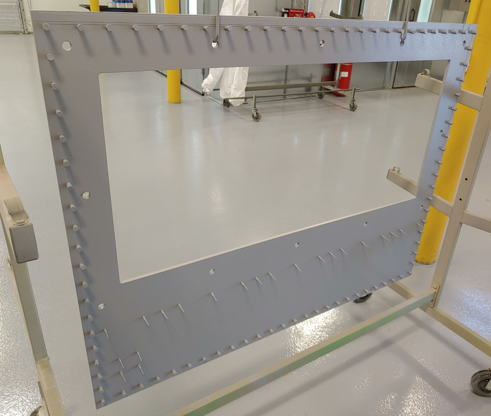Large gray rectangular frame with many small metal pieces, likely industrial, in a clean room.