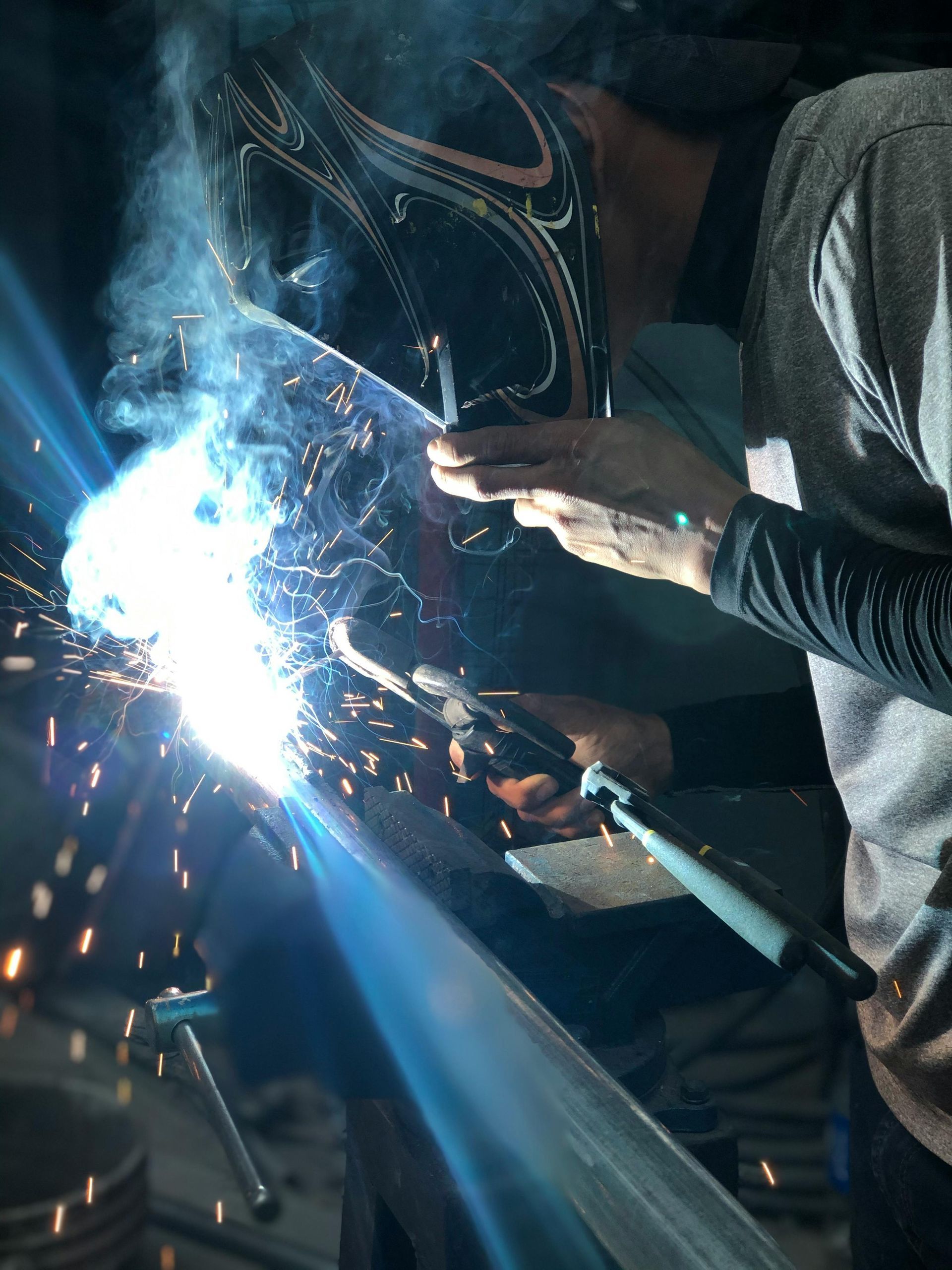 Person welding metal, bright sparks and blue light, wearing a welding mask in a workshop.